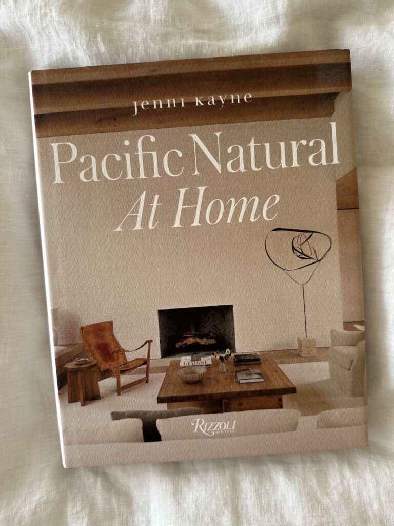 Pacific Natural at Home by Jenni Kayne, resting atop white linen bedding, offers effortless coastal-inspired design ideas for creating serene, stylish spaces.