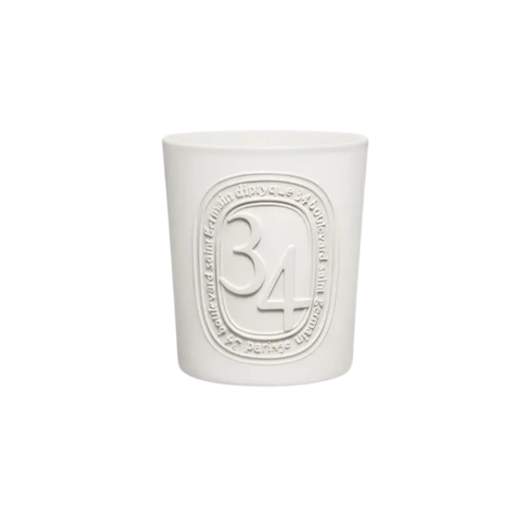 A 600g white porcelain candle from Diptyque's 34 Boulevard Saint Germain collection, featuring three wicks and the brand's emblematic oval seal. The candle emits a complex fragrance of moss, crushed blackcurrant leaves, spices, and floral notes, housed in a white opaline vessel.