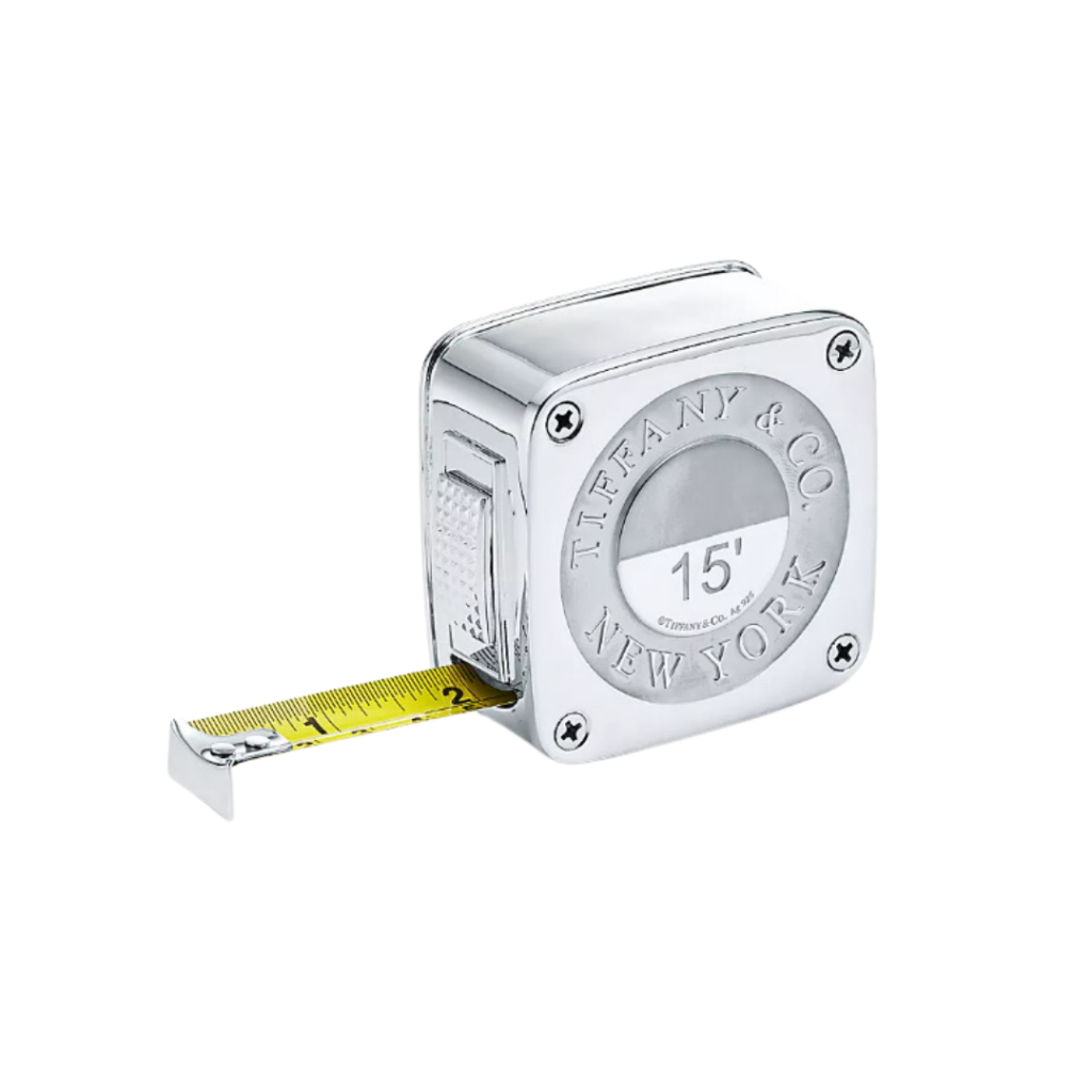 Tiffany & Co.'s Everyday Objects Tape Measure, encased in sterling silver with diamond-point accents, featuring a 15-foot retractable stainless steel tape marked in inches and metrics, blending luxury with functionality.