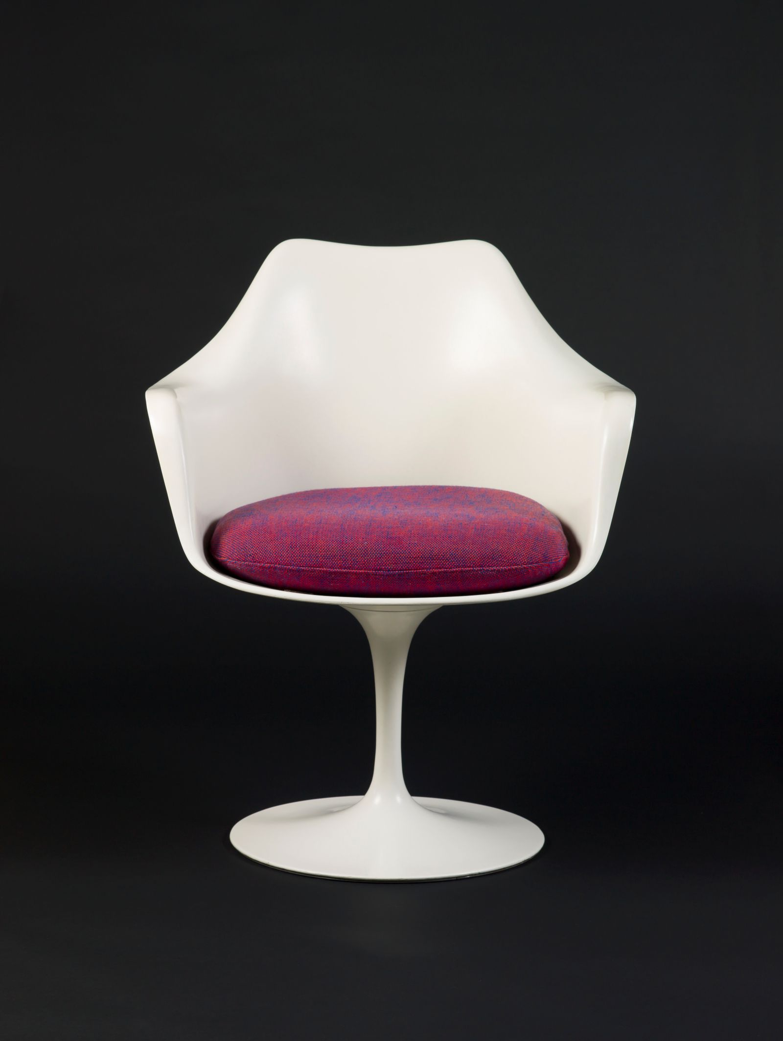 A striking front view of Eero Saarinen's classic white Tulip Chair, a celebrated piece brought to fruition by Knoll Associates under the influential direction of Florence Knoll, featuring a vibrant magenta seat cushion against a minimalist dark background.